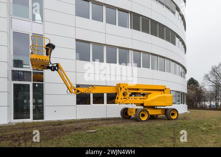 Una piattaforma di lavoro aerea gialla luminosa su uno sfondo bianco dell'edificio. Foto Stock