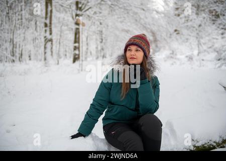 Un'immagine raffigurante una donna seduta su un terreno innevato in una foresta, che sembra premurosa. È vestita con una giacca invernale color ottanio e un multicolore Foto Stock