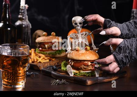 Le mani delle streghe vogliono prendere il Monster Burger sullo scheletro seduto. Perfetto antipasto per la festa di Halloween Foto Stock