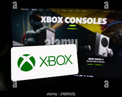 Persona con smartphone con logo della console videogiochi Xbox (Microsoft) davanti al sito Web. Mettere a fuoco il display del telefono. Foto Stock