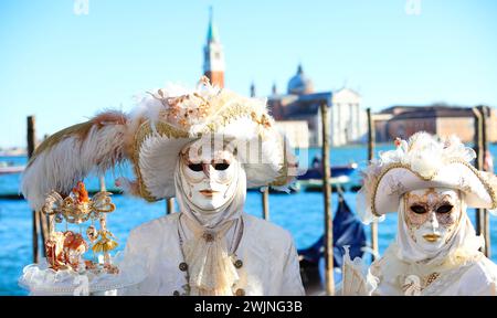 Venezia, VE, Italia - 13 febbraio 2024: Due persone con maschere bianche in riva al mare Foto Stock