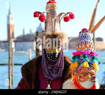 Venezia, VE, Italia - 13 febbraio 2024: Uomo e donna con enormi cappelli fantasiosi durante il carnevale veneziano in riva al mare Foto Stock