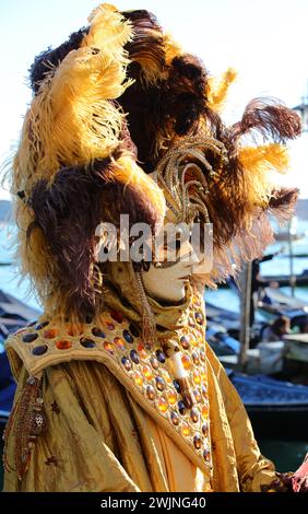 Venezia, VE, Italia - 13 febbraio 2024: Persona mascherata con un enorme copricapo con piume e decorazioni e abito fatto a mano durante il carnevale veneziano Foto Stock