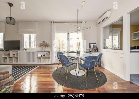 Bellissimo tavolo da pranzo circolare dipinto in bianco lucido con sedie rivestite in velluto blu che lo circondano Foto Stock