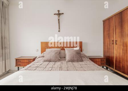 Camera da letto con testiera e mobili in legno verniciato, copriletto e cuscini coordinati e una croce cattolica sulle pareti Foto Stock