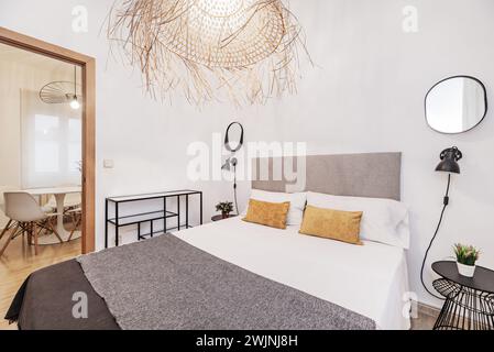 Una camera con letto matrimoniale con testiera rivestita in velluto grigio, grande lampada in vimini sul soffitto e comodini in metallo nero Foto Stock
