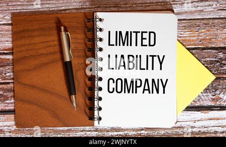 LLC- Limited Liability Company acronimo scritto in quaderno su sfondo in legno. Foto Stock