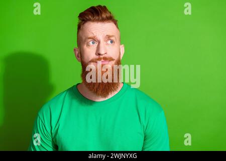 Ritratto di un ragazzo confuso con la barba rossa indossa un'elegante t-shirt con un look attento che offre uno spazio vuoto isolato su sfondo di colore verde Foto Stock