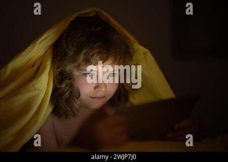 Bambino che guarda il tablet prima di dormire. Il bambino legge l'e-book. Il ragazzino guarda lo schermo del tablet in alto. Ragazzo che gioca un tablet sdraiato su un Foto Stock