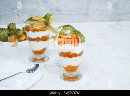 Due bicchieri di dessert stratificato con yogurt proteico e frutta fisalis Foto Stock