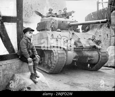 Guardate Yank Armor Roll By -- Un ragazzo tedesco siede sul lato di una strada a Zwisten, in Germania, incantato dallo spettacolo dei carri armati della nona divisione corazzata della prima Armata americana che si muovono attraverso la città. 9 aprile 1945. (Foto di William C. Allen, Associated Press Photo). Foto Stock
