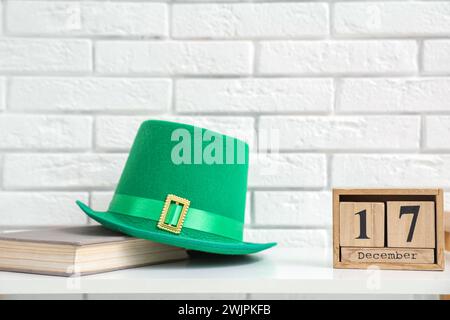 Cappello di leprechaun, calendario cubo e libro sul tavolo bianco, primo piano. St Festa di Patrick Foto Stock