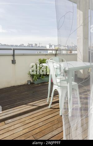 Un grazioso tavolo da giardino in metallo blu pastello con sedie abbinate su una terrazza urbana con pavimenti in legno, piante verdi e tende traslucide Foto Stock