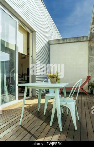 Un grazioso tavolo da giardino in metallo blu pastello con sedie abbinate su una terrazza urbana con pavimenti in legno Foto Stock