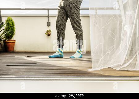 Gambe di un uomo che indossa pantaloni elastici con una stampa mimetica che cammina su una terrazza con pavimento in legno Foto Stock