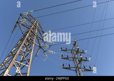 Alcune torri ad alta tensione che trasportano l'elettricità attraverso i loro cavi con isolatori a campana in una bella giornata con cieli limpidi Foto Stock