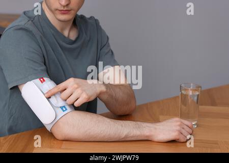 Uomo che misura la pressione sanguigna con il tonometro a un tavolo di legno all'interno, primo piano Foto Stock