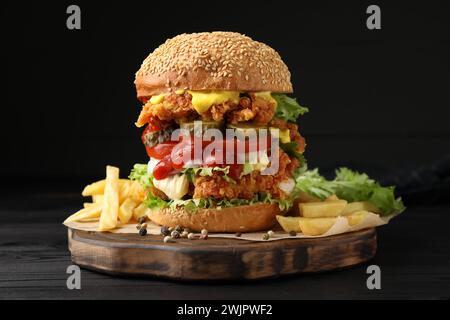Delizioso hamburger con polpette di pollo croccanti e patatine fritte su un tavolo di legno nero Foto Stock
