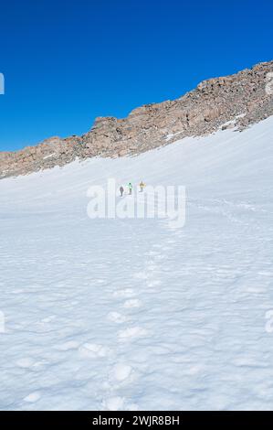 Un gruppo di persone è visto camminare attraverso un paesaggio innevato, circondato da formazioni rocciose glaciali e dal freddo cielo invernale Foto Stock