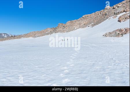 Un gruppo di persone è visto camminare attraverso un paesaggio innevato, circondato da formazioni rocciose glaciali e dal freddo cielo invernale Foto Stock