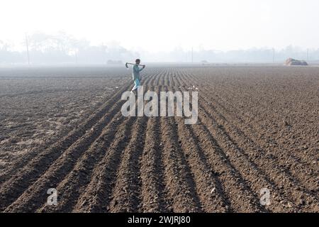 Munshiganj, Dacca, Bangladesh. 17 febbraio 2024. Gli agricoltori tornano a casa dopo aver preparato un campo a Munshiganj, Bangladesh, per seminare semi di patate. Le patate impiegano almeno 90 giorni per maturare dopo la semina. Patate intere o pezzi di patate possono essere utilizzati come semi. Un gruppo di lavoratori può raccogliere fino a 3.000 kg di patate al giorno. I campi sono meticolosamente organizzati, con file di patate ben allineate, promettendo un rendimento futuro che contribuirà al sostentamento e alla prosperità economica della regione. Le patate sono diventate un alimento base in molte parti del mondo e parte integrante di gran parte del Foto Stock