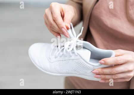 Donna che tiene scarpe sportive eleganti in interni, primo piano Foto Stock