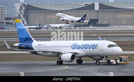 14 febbraio 2024, Assia, Francoforte sul meno: Mentre un aereo Lufthansa decolla, un aereo passeggeri Discover Airlines viene trainato da un rimorchiatore all'aeroporto di Francoforte. Fino allo shock della corona, l'aeroporto di Francoforte conosceva solo la crescita. In occasione del 100° anniversario della società operativa Fraport, le prospettive economiche si sono riprese in modo significativo. Foto: Arne Dedert/dpa Foto Stock