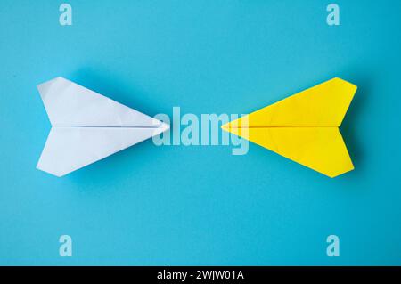 Vista dall'alto di un origami di carta bianca e gialla che vola l'uno verso l'altro su sfondo blu. Foto Stock