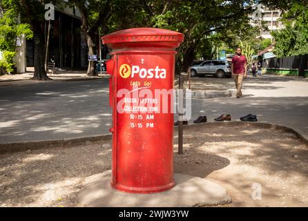 Scarpe sul marciapiede accanto a una scatola a colonna rossa in stile coloniale britannico, o una cassetta delle lettere, utilizzata da posta Tanzania per la strada nel centro di Dar es Salaam, Tanza Foto Stock