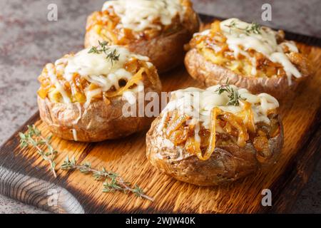 Le patate al forno con cipolla francese si ispirano alla classica zuppa e sono ricoperte da cipolle caramellate e un primo piano di formaggio sulla tavola di legno sul tavolo. Foto Stock