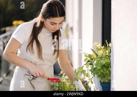 Donna attraente inizia a sbarcare sul balcone. Giovane donna in tute a strisce leggere piantando Foto Stock