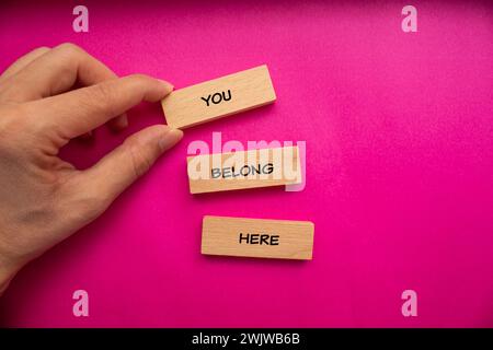 Qui appartenete a parole scritte su blocchi di legno con sfondo rosa. Simbolo commerciale concettuale. Copia spazio. Foto Stock