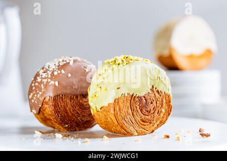 Croissant di fusione, pasticceria dolce Cromboloni. Dessert di New York. Pasta sfoglia rotonda ripiena di panna e glassata con cioccolato bianco al latte o pistacchio Foto Stock