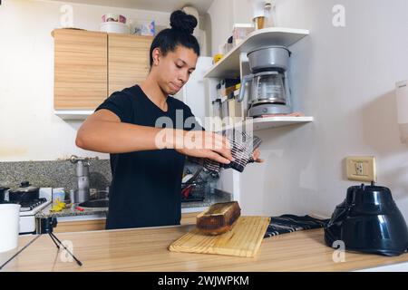 Il giovane latino in cucina a casa, sformando, tirando fuori la torta appena sfornata dalla muffa, mettendola sul tagliere sul tavolo. Foto Stock