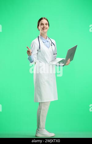 Una dottoressa donna, a tutta lunghezza, su sfondo verde, usa un notebook Foto Stock