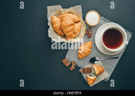 Croissant appena sfornati avvolti in carta da imballaggio su un tavolo di legno per colazione. sfondo scuro. posiziona per testo. L'ora del caffè. Cottura al forno. croissant. T Foto Stock