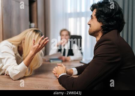 Coppia sposata che litiga di fronte a uno psicologo familiare. Moglie arrabbiata che litiga con il marito triste durante la consulenza di coppia. Una coppia infelice Foto Stock