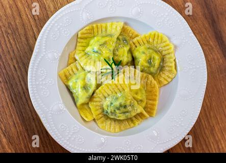 Serve ravioli fatti in casa con salsa al burro di mucca in un piatto bianco sul tavolo Foto Stock