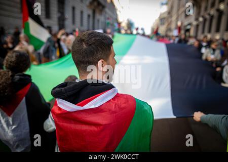 Madrid, Spagna. 17 febbraio 2024. Un uomo con una bandiera palestinese guarda i manifestanti sventolare una gigantesca bandiera palestinese durante una manifestazione. Centinaia di persone hanno dimostrato ancora una volta nel centro di Madrid di chiedere un cessate il fuoco da parte dello Stato di Israele contro la Palestina e di fermare la vendita di armi da parte del governo spagnolo a Israele. (Foto di David Canales/SOPA Images/Sipa USA) credito: SIPA USA/Alamy Live News Foto Stock