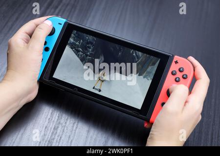 Ragazza che gioca a Tomb Raider Remastered Starring Lara Croft su console Nintendo Switch in modalità portatile, messa a fuoco selettiva su uno schermo Foto Stock