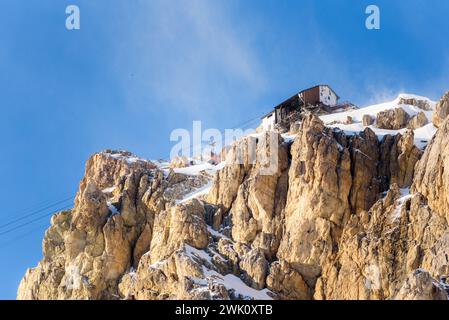 Cabina della funivia che si avvicina alla stazione superiore su una cima rocciosa innevata delle Alpi in una soleggiata giornata invernale Foto Stock