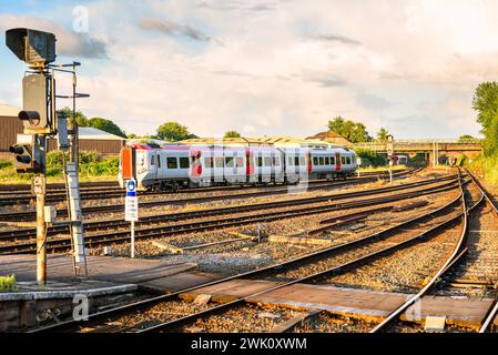 Treno passeggeri diesel in partenza dalla stazione al tramonto in estate. Altri due treni sono visibili in lontananza. Foto Stock