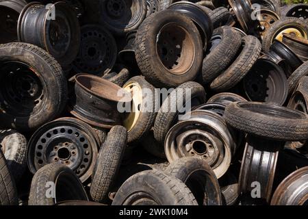 Pile di pneumatici assortiti per auto e camion scartati e cerchioni in acciaio presso il deposito rottami per il riciclaggio dei metalli. Foto Stock