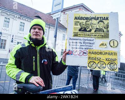 Budapest, Budapest, Ungheria. 17 febbraio 2024. Un attivista ungherese con la sua bici, reca un cartello con scritto "Partito della Guerra" di fronte a Varkert, dove il primo ministro ungherese VIKTOR ORBAN ha tenuto il suo discorso annuale e commentato tre dimissioni del presidente ungherese, KATALIN NOVAK; l'ex ministro e leader della Chiesa riformata ungherese, ZOLTAN BALOG e l'ex ministro della giustizia, JUDIT VARGA, a seguito dell'esposizione di un uomo perdonato l'anno scorso per aver coperto la pedofilia in una casa per bambini. La rivelazione ha causato imbarazzo e offuscato l'immagine della zona sicura ungherese e l'immagine di alto valore familiare. Foto Stock