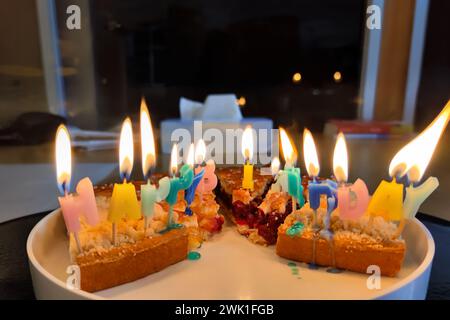 Torte di compleanno disordinate colorate e colorate, che si fondono con le candele di buon compleanno su fette di torta visualizzate su un piatto, per un felice disastro di compleanno. Foto Stock