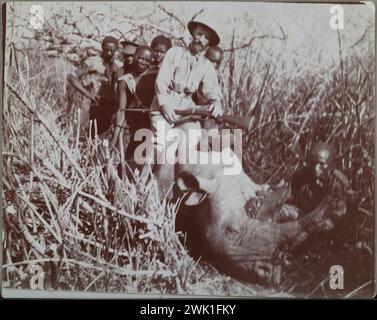 Vintage Photography, Kenya c. 1910. L'artista norvegese Akseli Gallen-Kallela in caccia alla caccia con la gente del posto in piedi su un rinoceronte caduto. Ha vissuto con la sua famiglia nel 1909-10 nell'Africa Orientale Britannica, oggi Kenya. Le pelli e le corna di diversi animali sono state recuperate e successivamente donate all'Università di Helsinki. Foto Stock