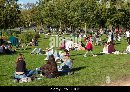 La gente gode del bel tempo su un prato vicino all'acqua nel Vondelpark di Amsterdam. Foto Stock
