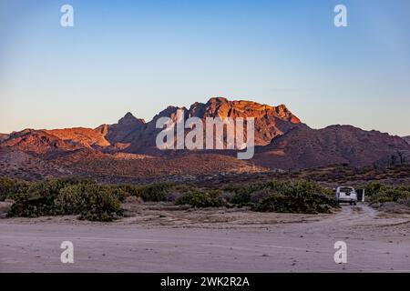 Paesaggio desertico messicano con alberi di ginepro e macchia, imponente formazione rocciosa di montagna illuminata dal sole sullo sfondo, auto parcheggiata su sabbia, soli Foto Stock
