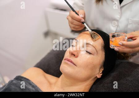 Cosmetologo del raccolto che applica il trattamento sul viso del cliente Foto Stock
