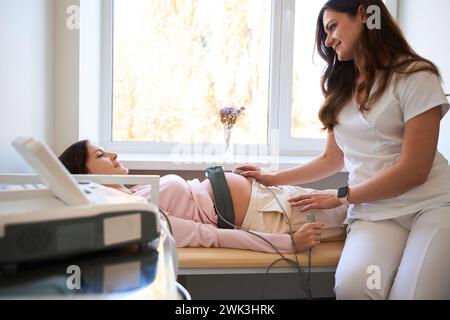 Esame ostetrica pancia di una bella donna incinta con scansione CTG Foto Stock